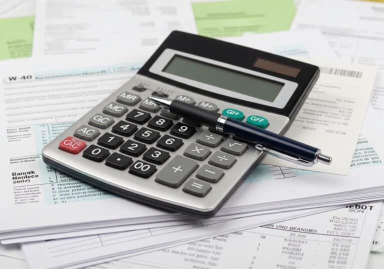 a close-up image of a calculator and a pen on top of a pile of financial documents, symbolizing tax preparation